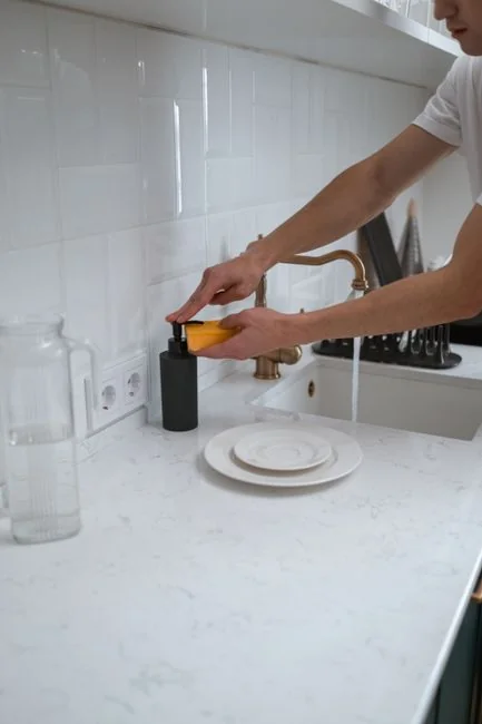 Close-up view of a hand wiping a window outdoors with a squeegee while wearing yellow gloves.