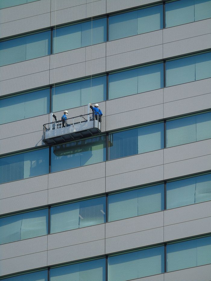 Two workers are cleaning windows on the facade of a modern glass building from a suspended platform.